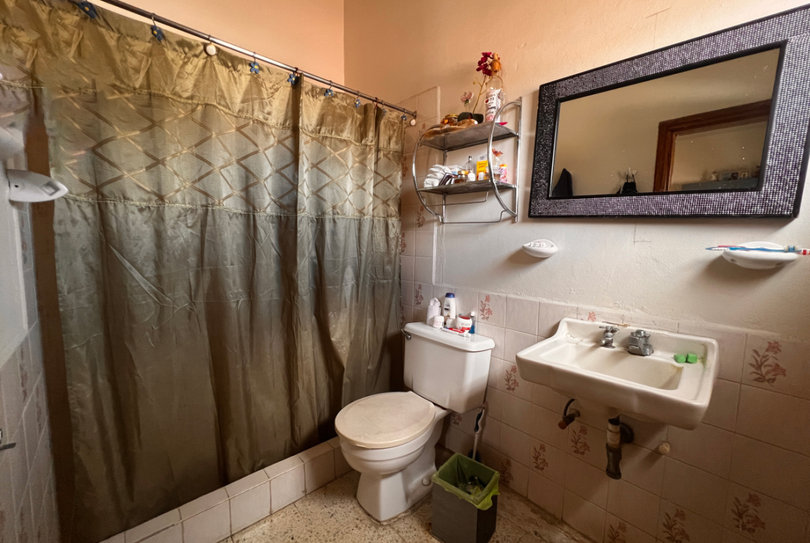 Baño de la casa con su inodoro, lavamanos y ducha con cortina color verde.