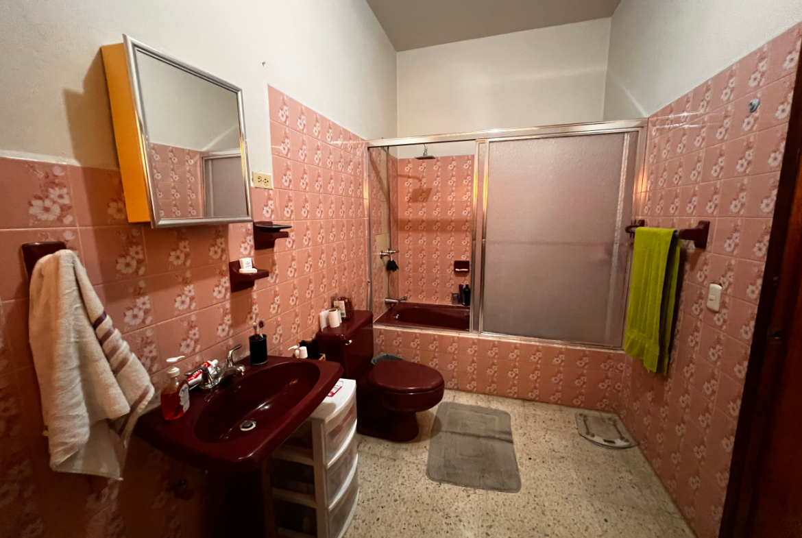 Baño de la habitación principal con su inodoro, lavamanos y tina con puerta de acrílico.