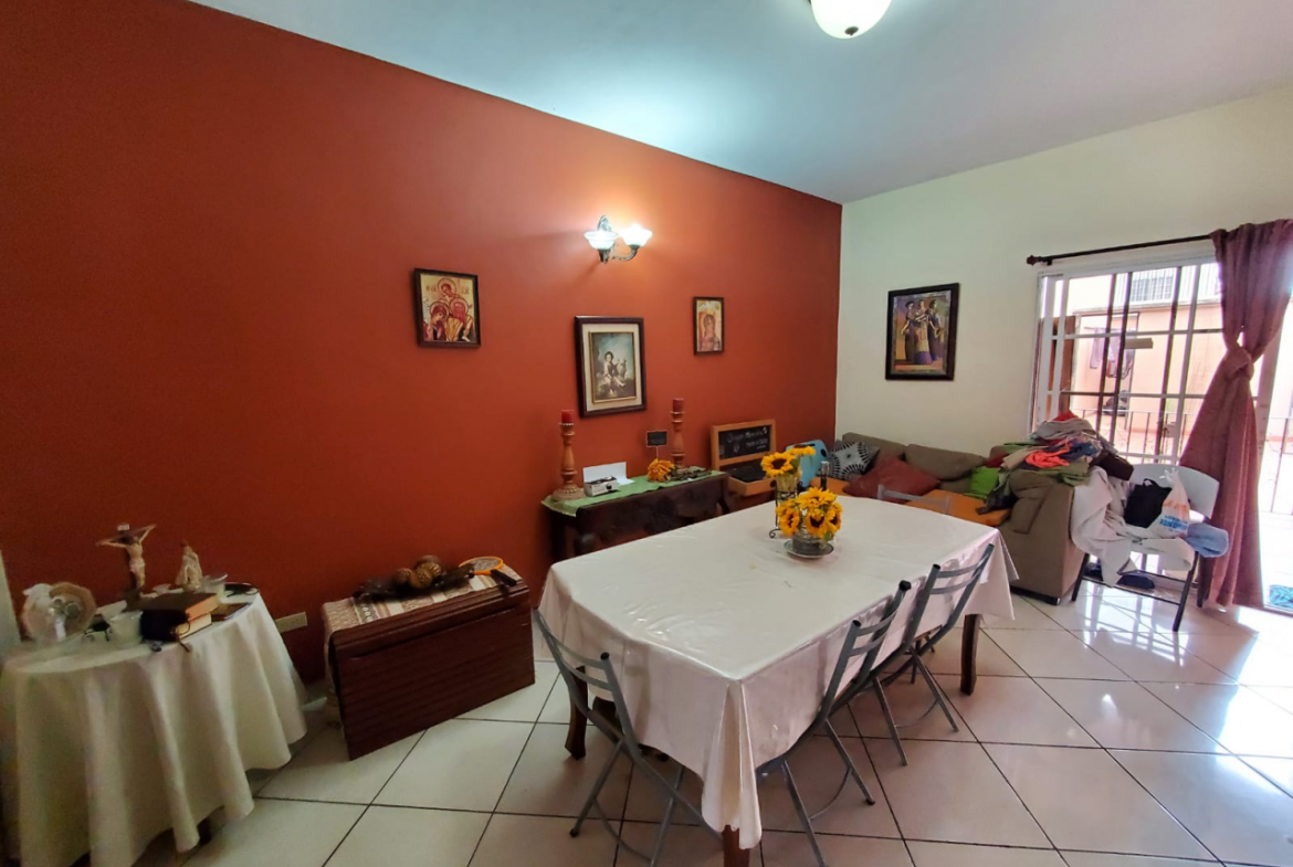 Área de la casa iluminada con un comedor de 6 sillas con un centro de flores, cuadros de pintura y un sofá en la zona sur de la ciudad.