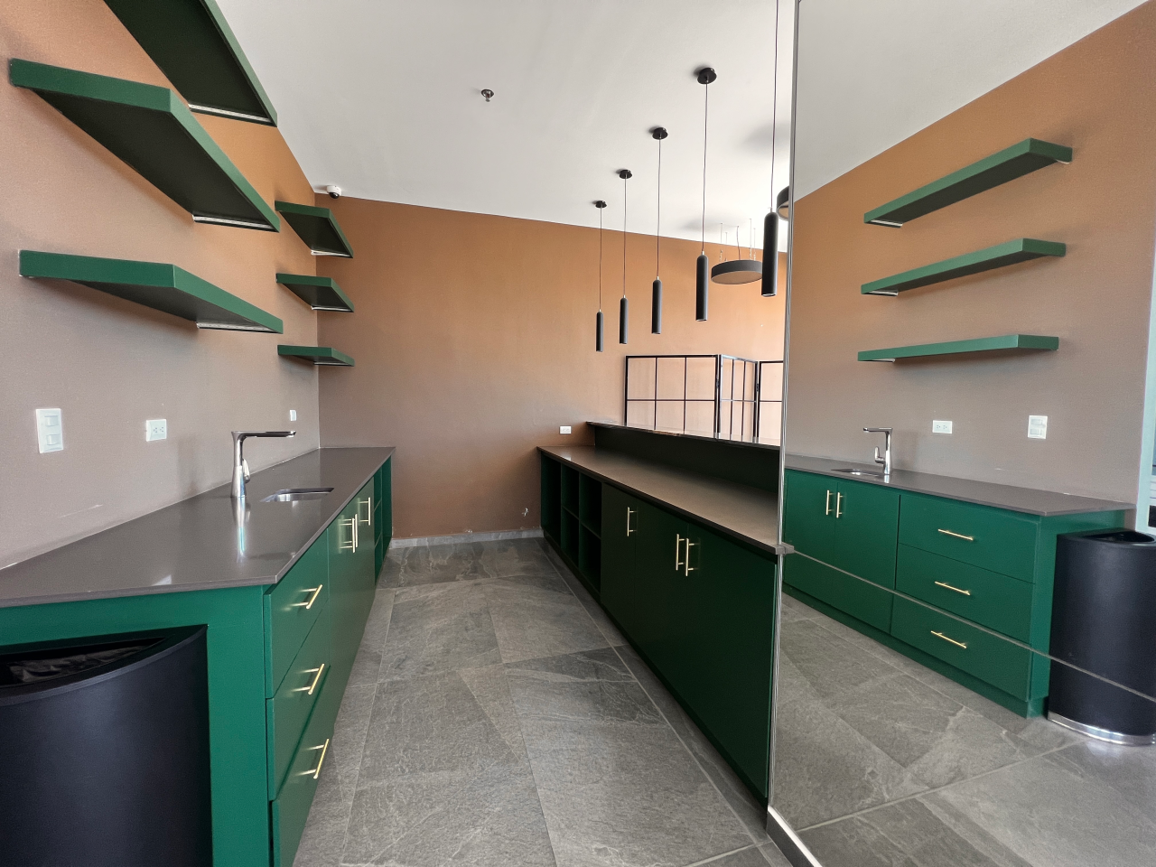 Área social de torre Agalta con muebles de cocina color verde y plancha de granito color negro, paredes color café claro, repisas y lámparas colgantes.