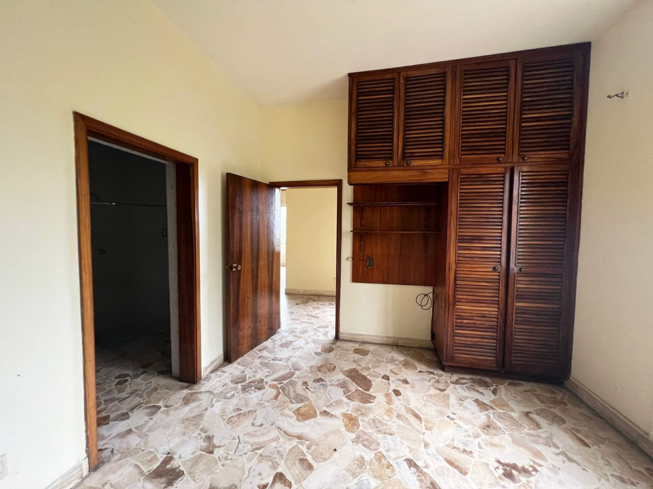 Habitación con closet de madera, pared color amarillo, baño privado con techo de tabla yeso.