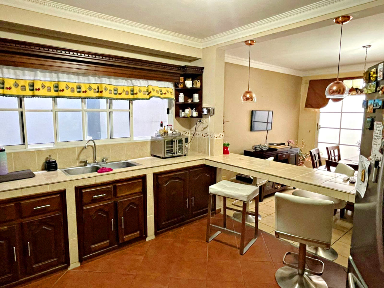 Hermosa cocina amueblada, con cocinera y desayunador, con una amplia ventana corrediza para que fluya el aire por toda la casa,, con suelo de caramica color naranja rojizo.