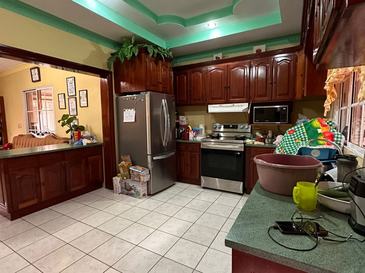 Area de cocina, con paredes de color amarillo suave, suelo de ceramica color blanco, muebles de color cafe barnizados, con area de lavado y espacio para colocar linea blanca.