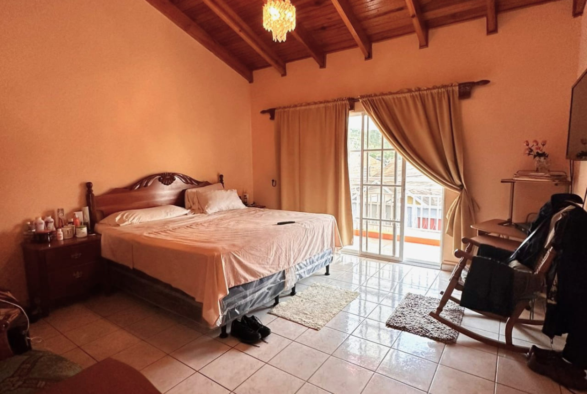 Área de dormitorio con paredes de color carmin, techo de madera, sujujelo de ceramica de color blanco, cama matrimonia, una puerta deslizable que brinda acceso al balcón.