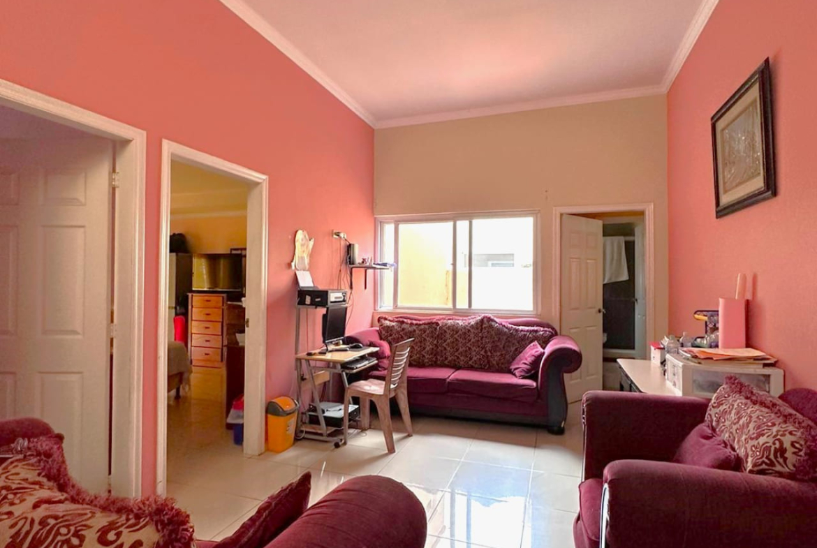 Segunda area de sala con paredes de color salmon, suelo de ceramica, muebles de tela color rojos a juegom con una pequeña área de estudio.