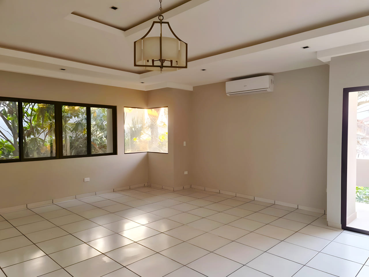 Habitación amplia con aire acondicionado, lámpara colgante, puerta corrediza con piso porcelanato y techo color blanco.