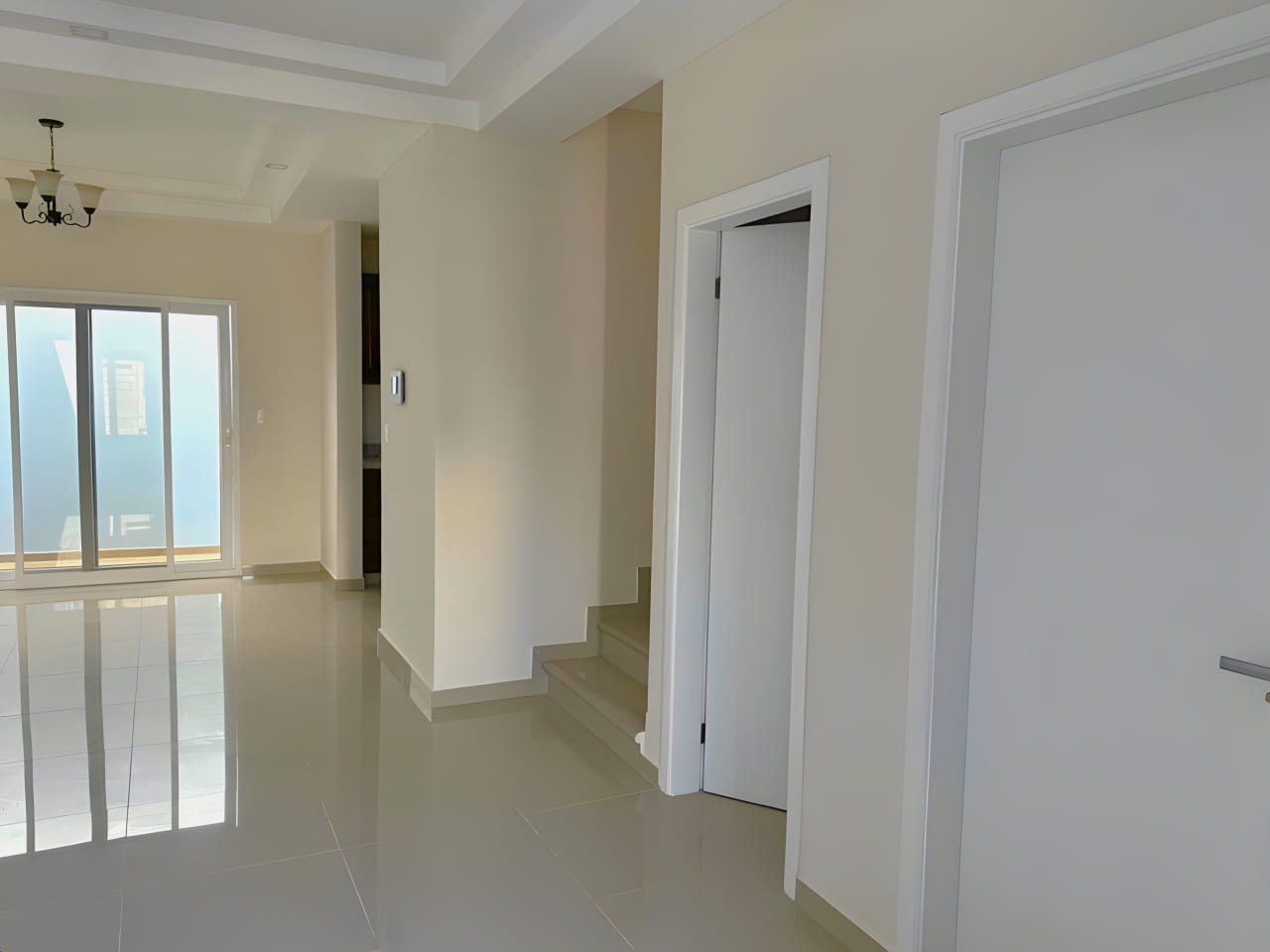 Área de acceso a dos habitaciones y cocina, con puertas de color blanco, suelo de porcelanta, puerta corrediza al fondo que brinda acceso al eterior de la casa.