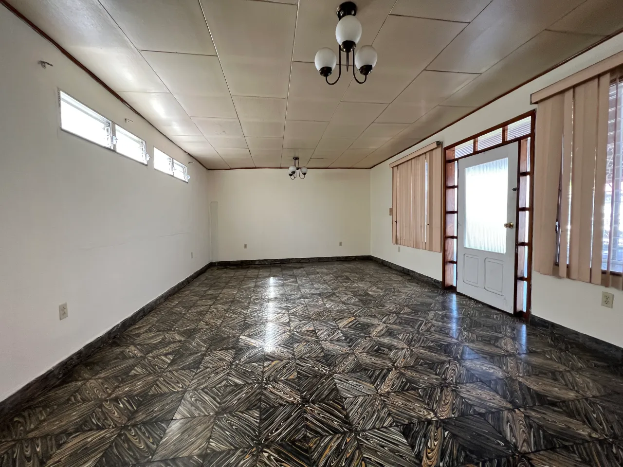 Habitación amplia con piso de ceramica oscura, paredes color beige con techo de tabla yeso junto a una puerta con acceso a la terrza