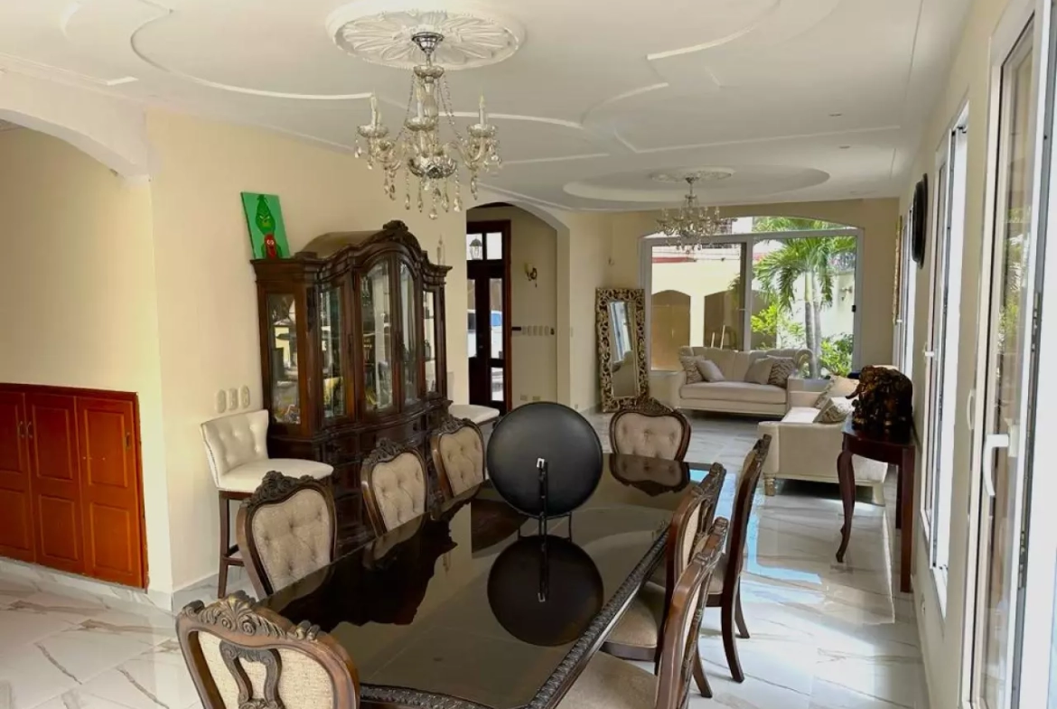 El área de comedor cuenta con una mesa amplia con 8 sillas, de fondo podemos observar la sala, acceso a la cocina y de fondo la parte de jardín.