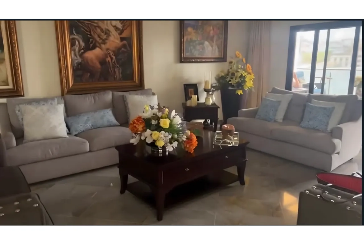 Sala de estar con cerámica de madera, mueble de color blanco, cuadros de pintura en la pared y una mesa de centro con ramos de flores.