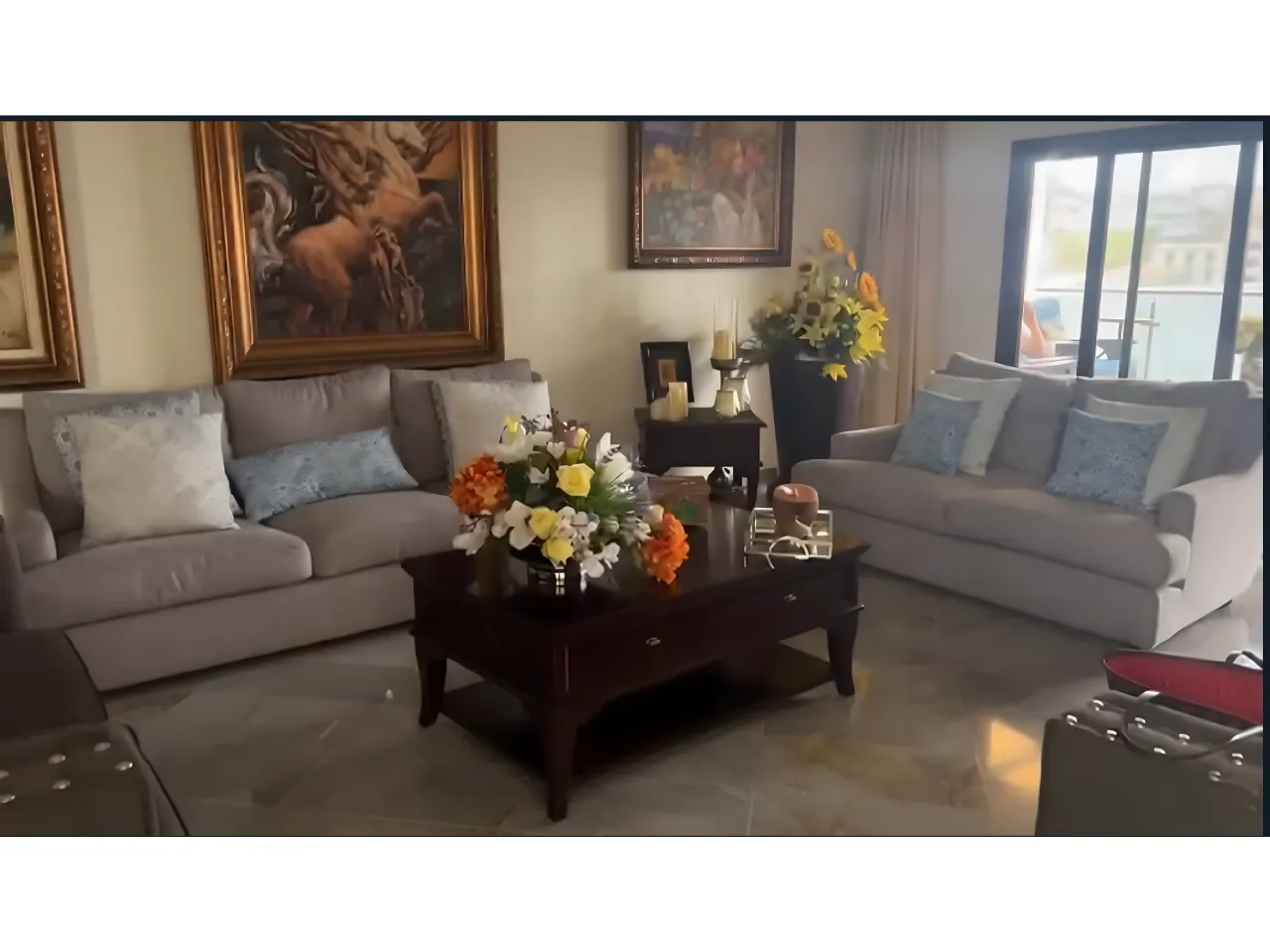Sala de estar con cerámica de madera, mueble de color blanco, cuadros de pintura en la pared y una mesa de centro con ramos de flores.