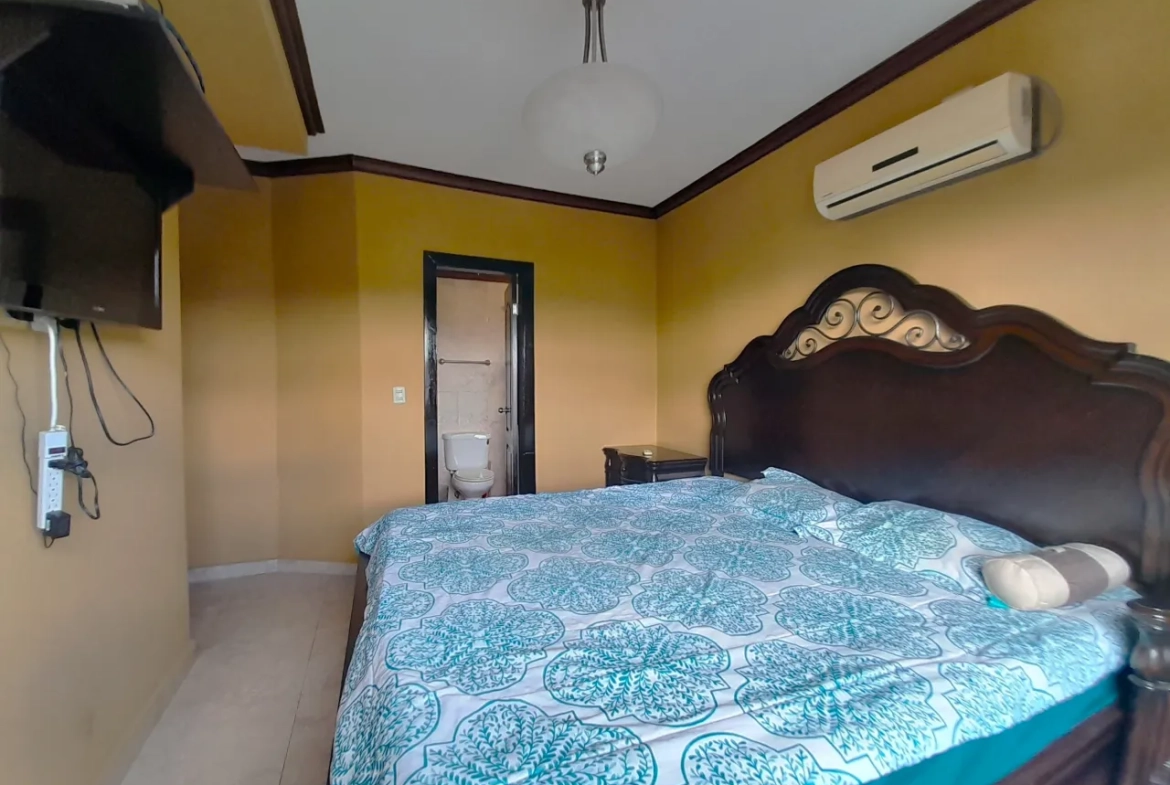 Una de las habitaciones cuenta con una cama matrimonial, aire acondicionado, baño privado, paredes de color amarillo, televisor colgado en la pared.