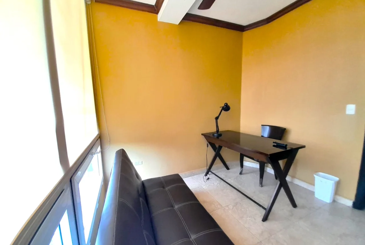 La área para estudio cuenta con mesa de madera, lampara de color negro, silla a juego y un sofá de cuero negro.