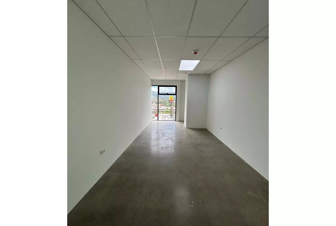 Oficina en alquiler con paredes color blanco, piso de cemento pulido y una ventana con vista al blvd. suyapa.