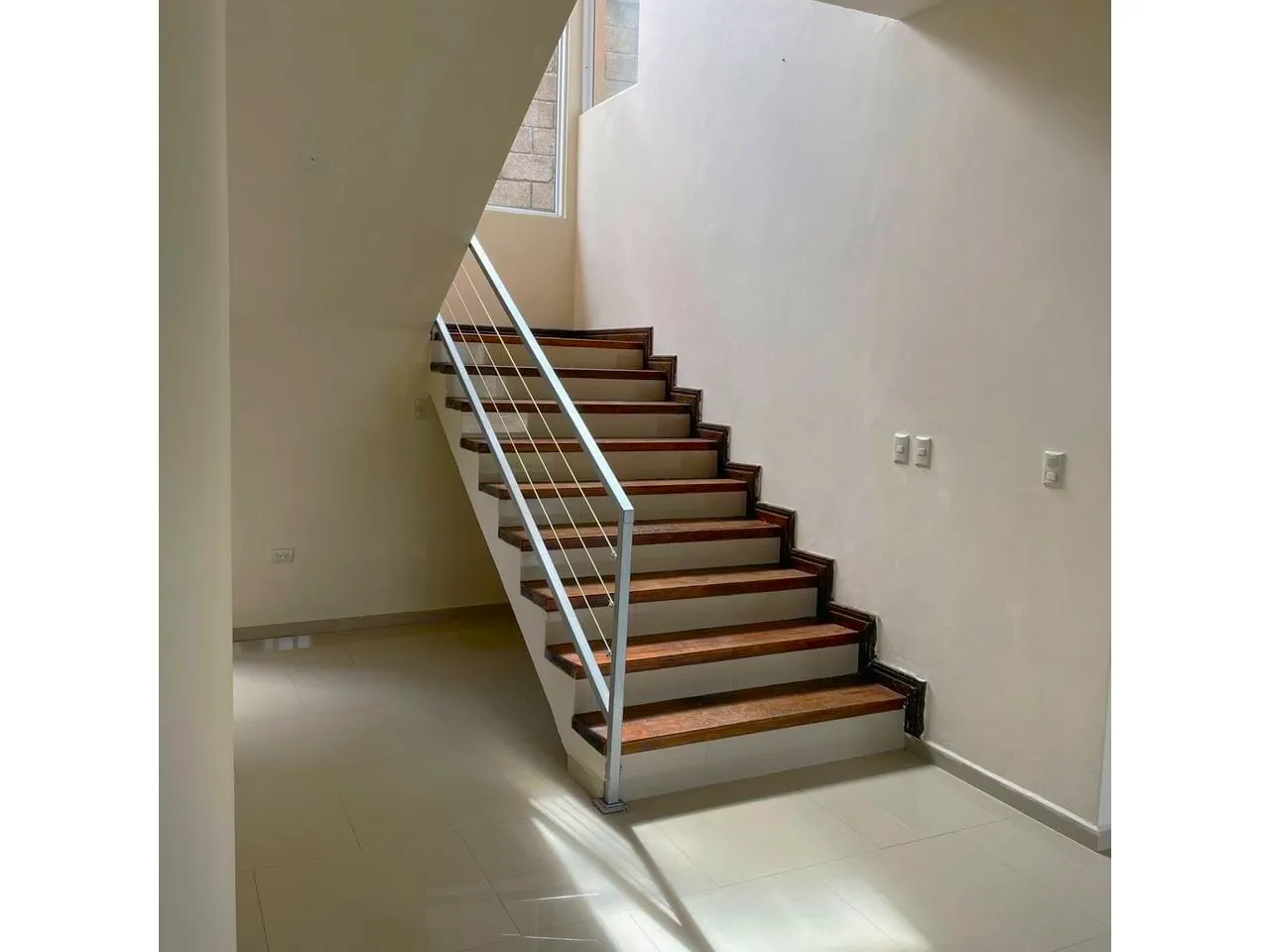 Escaleras decoradas con madera, paredes de color claro, suelo de porcelalanto que dan acceso a las 2 habitaciones del nivel superior.