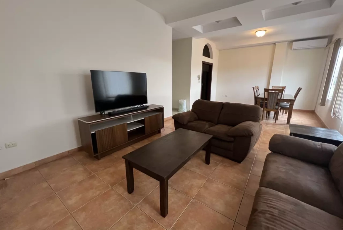 Sala de estar con muebles y una mesa de centro color café. Enfrente un mueble de madera con un televisor plasma.