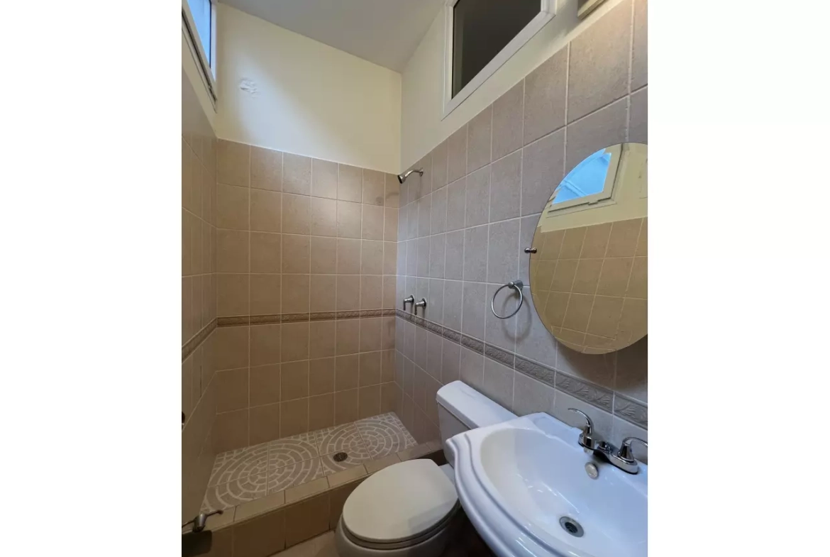 Baño secundario con inodoro, lavamanos, espejo ovalado en la pared y una bañera.