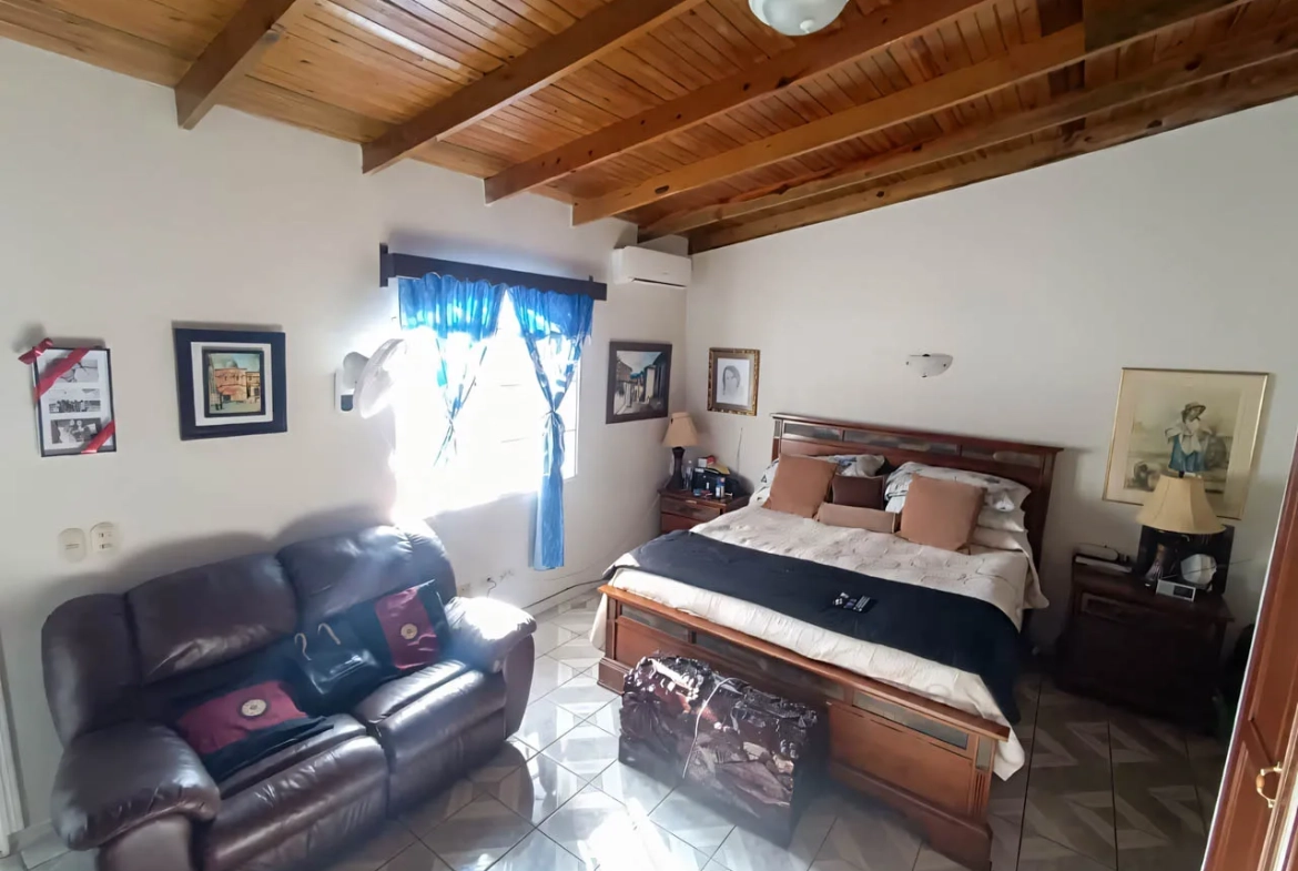Una de las habitaciones cuenta con una amplia cama matrimonial, un sofá de cuerina, una ventana con cortinas de color azul que permiten una hermosa iluminación al interior.
