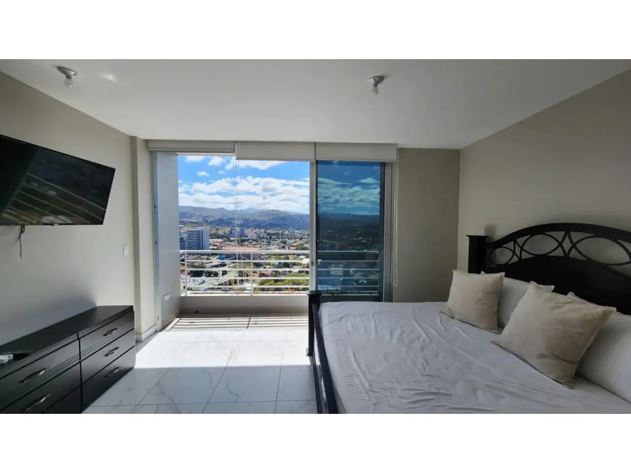 El cuarto principal cuenta con una cama amplia, televisor colgado en el suelo con una mesa y un balcón con hermosa vista