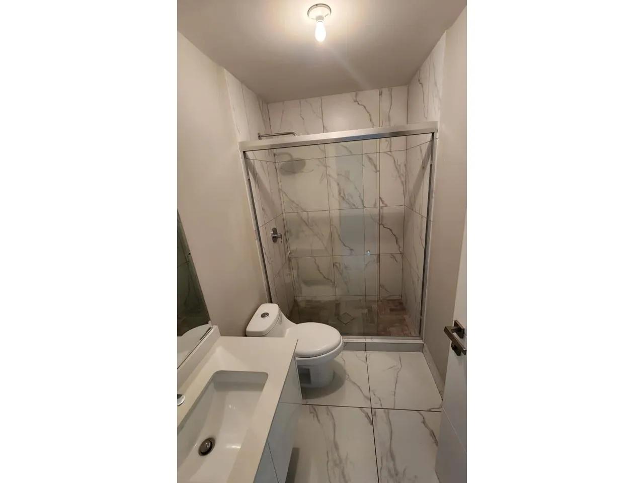 Uno de los baños cuenta con ducha con puertas corredizas de vidrio, retrete de color blanco y lavamanos con espejo amplio
