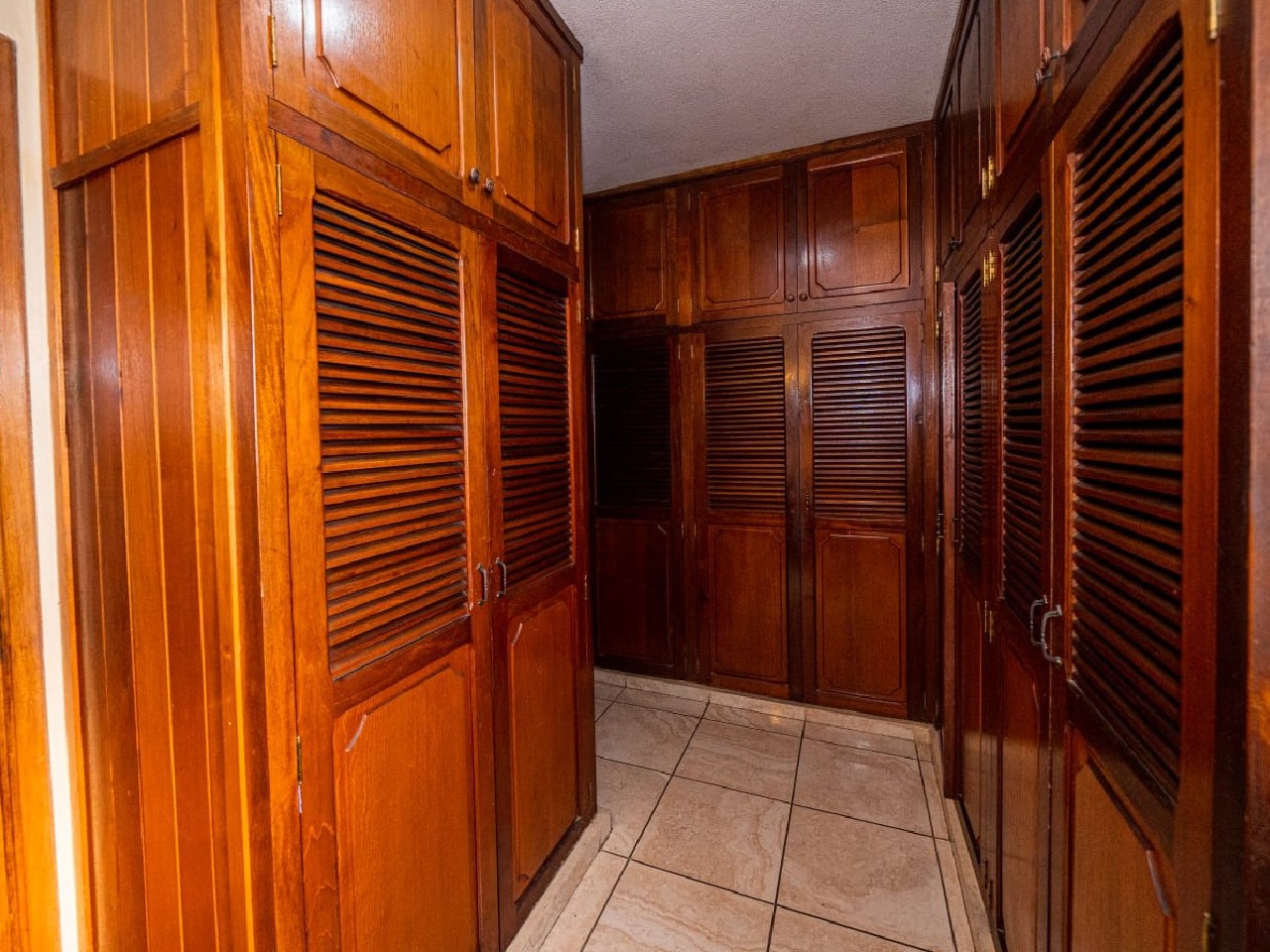 Un walk-in closet amplio de madera color café con varios espacios para acomodar tus pertenecias