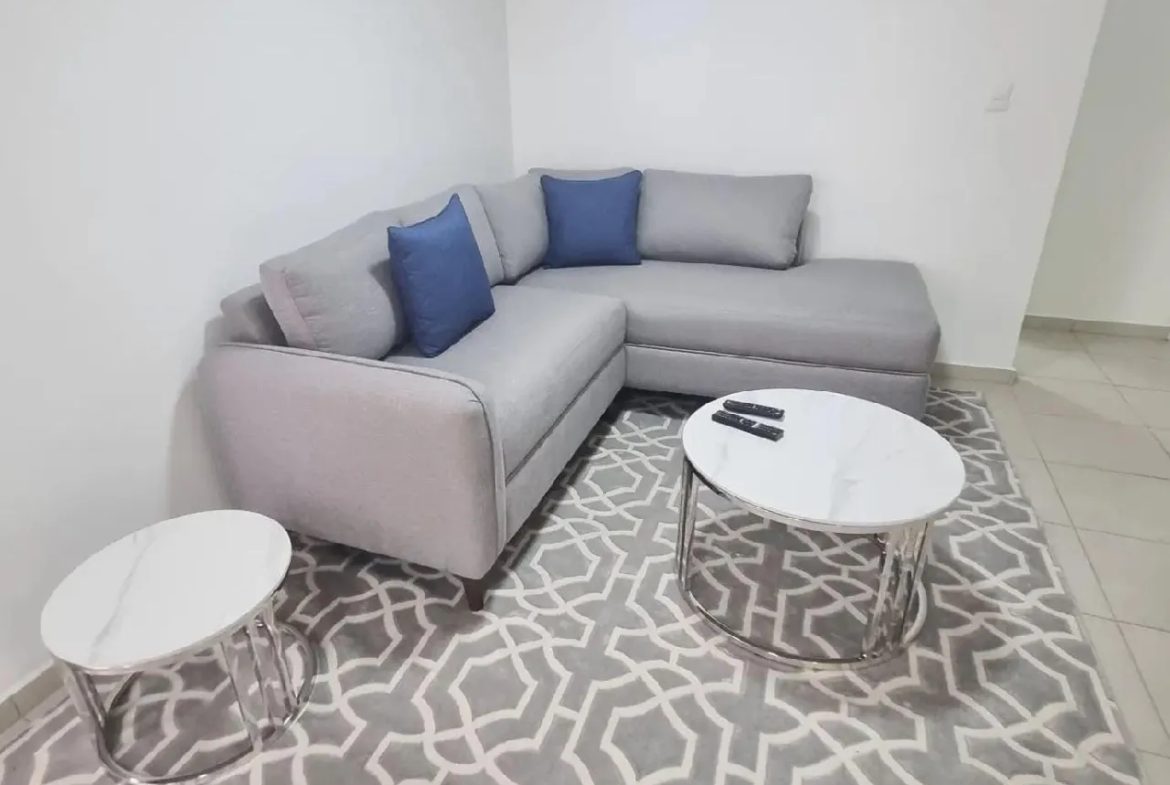 La sala ofrece un sofá en forma de L con cojines de color azul para dar más visibilidad a este espacio, también cuenta con 2 mesas redondas que puedes acomodar a tu gusto.
