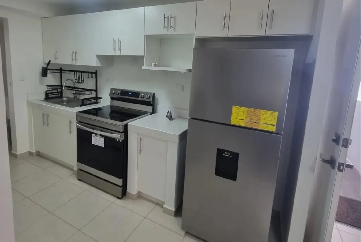 La cocina se encuentra totalmente equipada, cuenta con un refrigerador, estufa, escurridor de platos y muebles de color blanco.